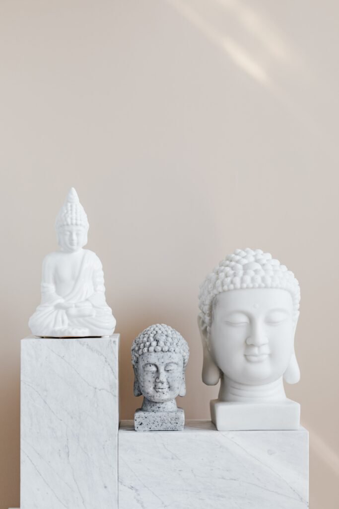 Set of various gypsum and stone Buddha sculptures placed on white marble shelf against beige wall as home decoration element and religion symbol